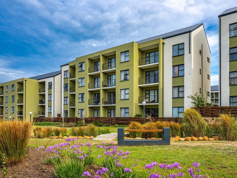 A view of the rear apartment building facade featuring multiple balconies, modern architectural design, and well-maintained landscaped garden areas.