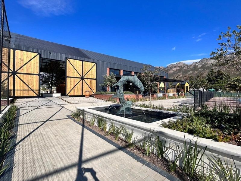 A well-maintained outdoor courtyard featuring a decorative water fountain, paved walkways, and modern industrial-style building architecture with large wooden sliding doors.