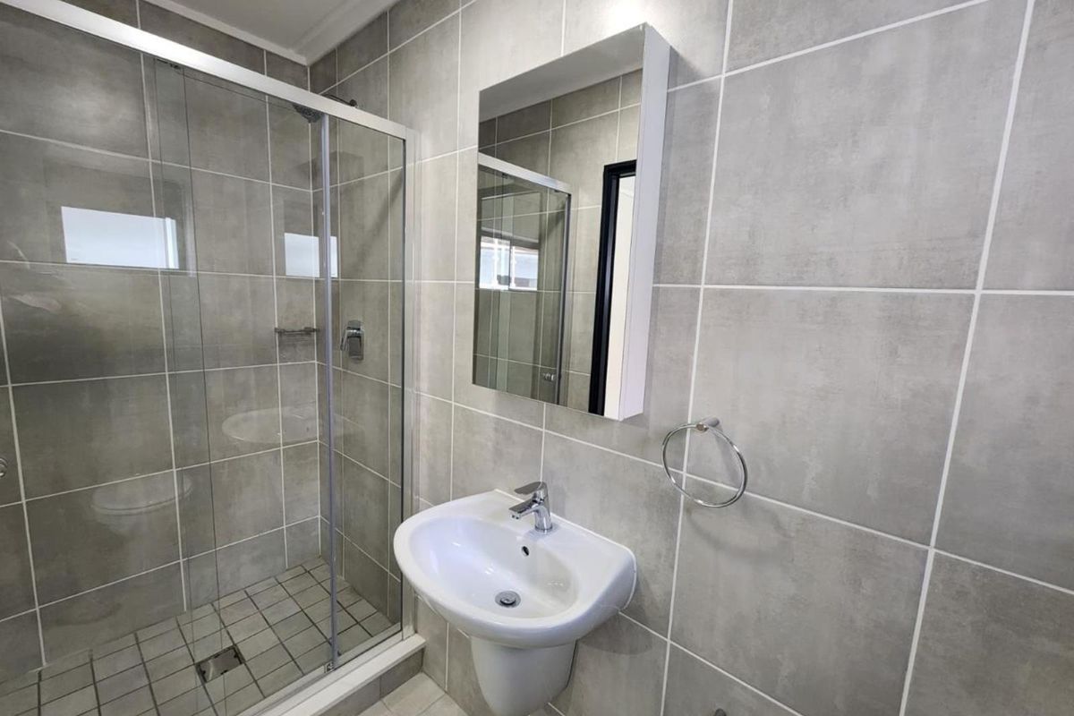 A modern, clean bathroom featuring a glass shower enclosure, pedestal washbasin, and neutral grey ceramic wall tiling.