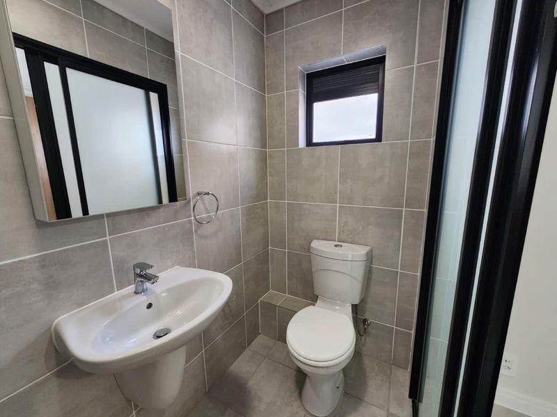 A modern, well-maintained bathroom featuring neutral wall and floor tiles, a pedestal washbasin, and a toilet.