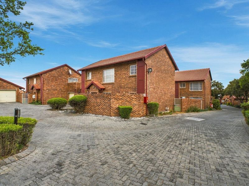 Exterior view of a face-brick apartment complex featuring a paved driveway, tiled roofing, and established garden landscaping within a secure residential estate.