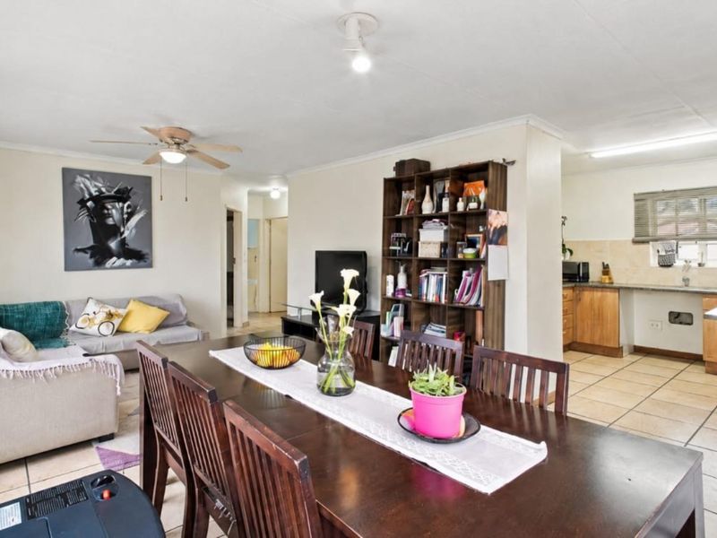 Open-plan living and dining area featuring tiled flooring, a ceiling fan, and an adjoining kitchen with functional cabinetry and counter space.