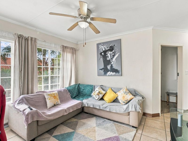 A bright living room featuring tiled flooring, a ceiling fan, and large grid-pattern windows that provide natural light.