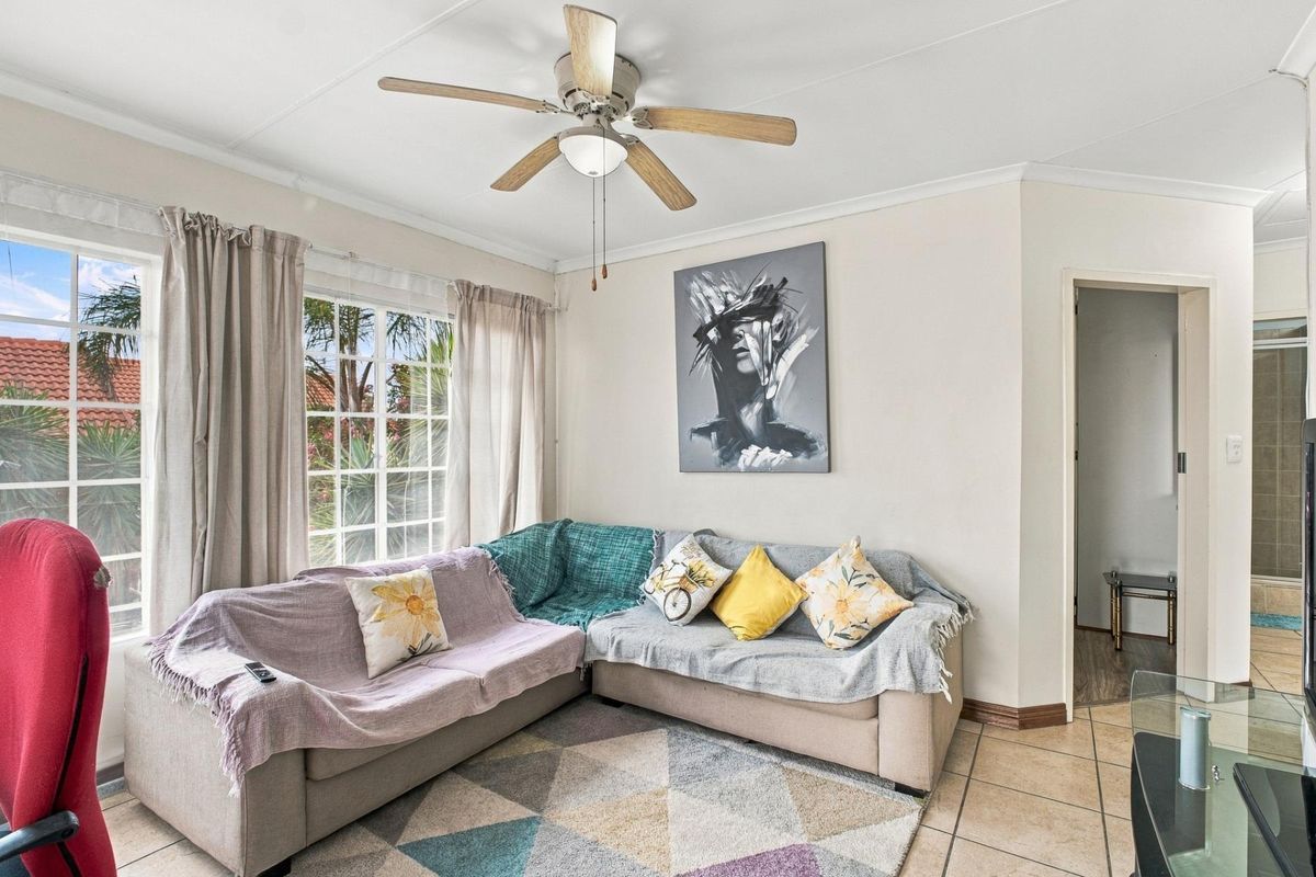 A bright living room featuring tiled flooring, a ceiling fan, and large grid-pattern windows that provide natural light.