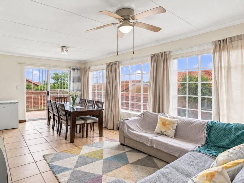 Spacious open-plan living and dining area featuring tiled floors, a ceiling fan, and large windows providing ample natural light with access to a balcony.