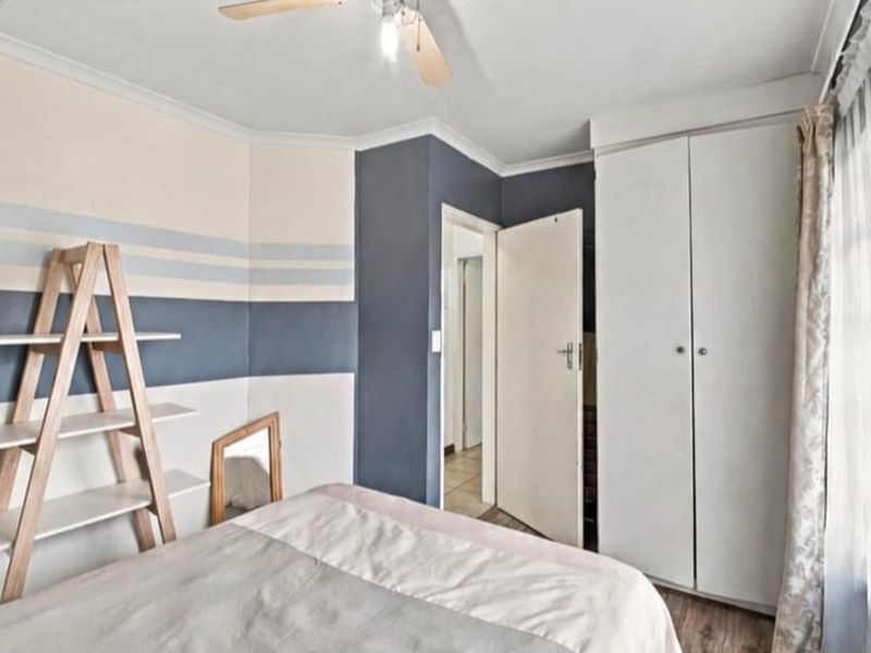 A bedroom featuring built-in cupboards, a ceiling fan, and laminate flooring, with neutral wall paint and coving details.