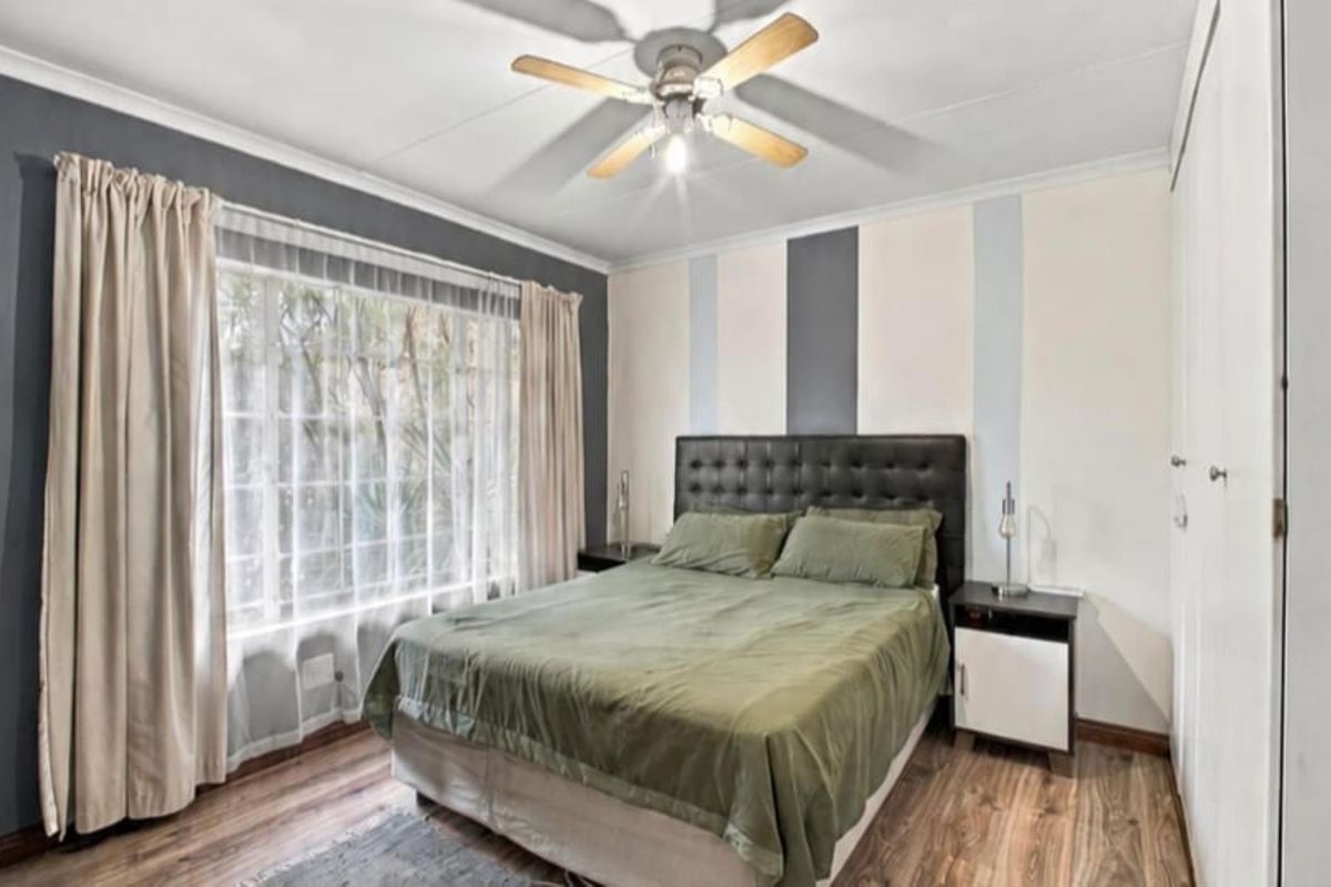 A well-lit bedroom featuring laminate flooring, a ceiling fan, and built-in storage cupboards.
