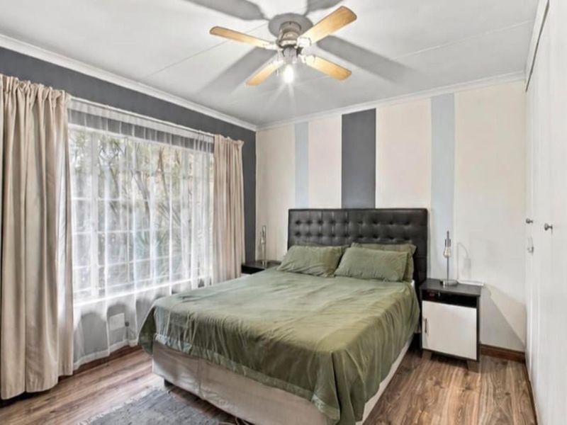 A well-lit bedroom featuring laminate flooring, a ceiling fan, and built-in storage cupboards.