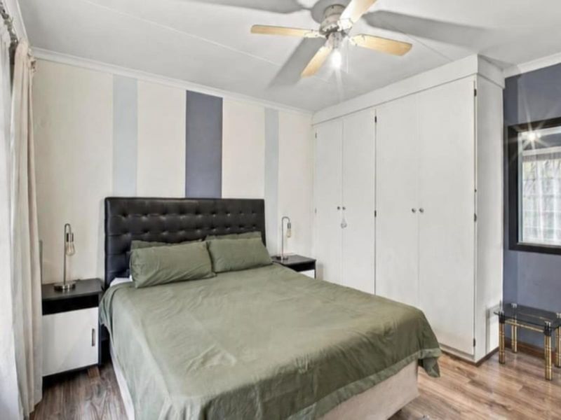 A well-proportioned bedroom featuring laminate flooring, a ceiling fan, and extensive built-in cupboard storage.