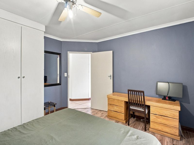 A bedroom featuring built-in wardrobes, a ceiling fan, and blue accent walls, providing a functional space with neutral flooring.
