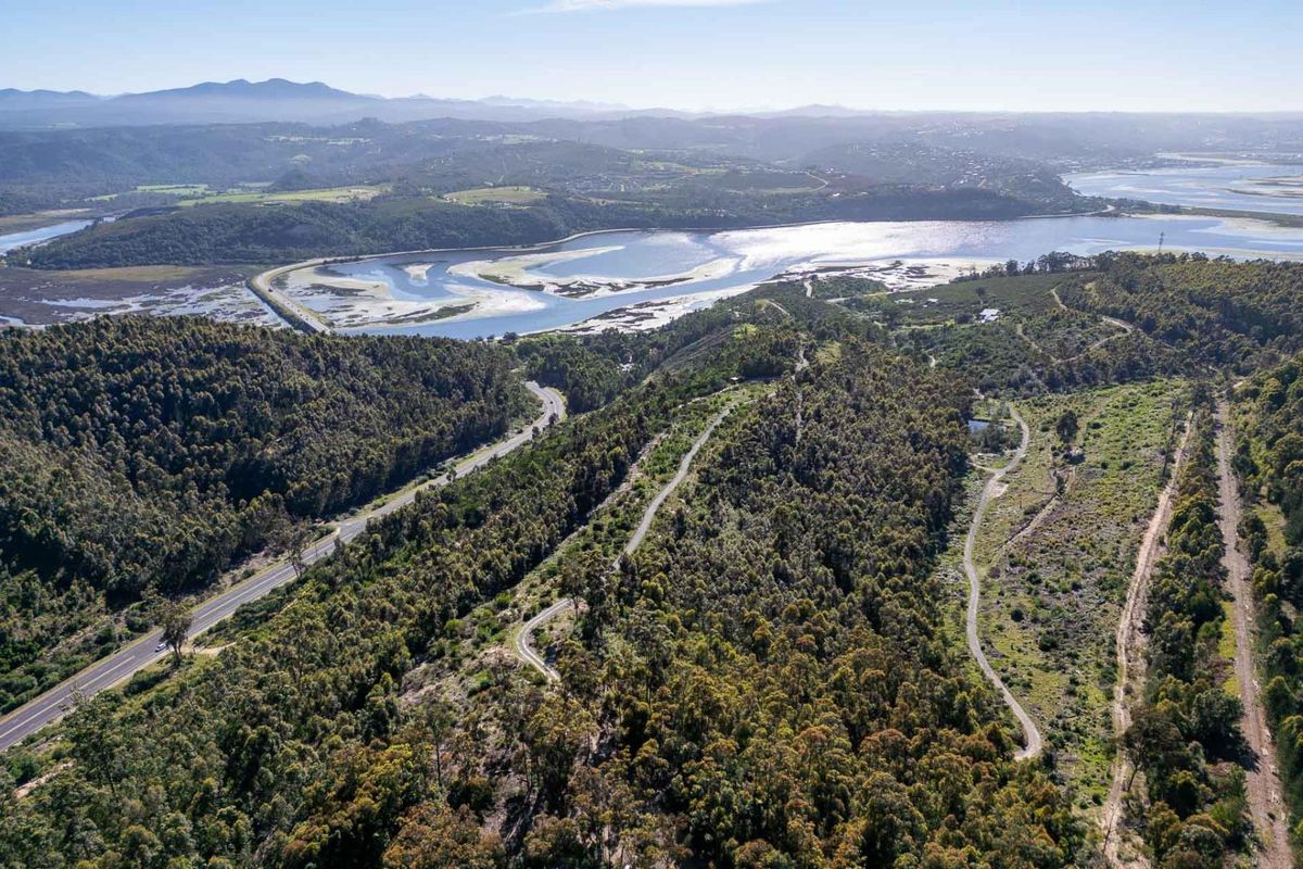 An expansive aerial view of the farm property, showcasing the surrounding natural landscape, forest, and proximity to the nearby estuary and road network.
