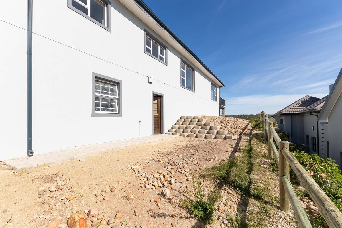 Rear exterior view of the property featuring a paved walkway, concrete block steps, and a timber fence, with unfinished landscaping area.