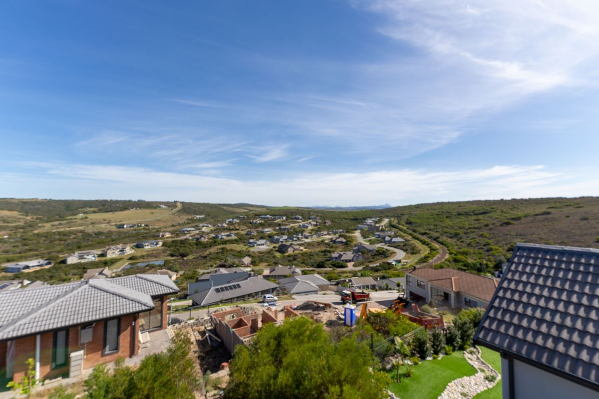 An elevated aerial view showcasing the surrounding residential estate, landscape, and neighboring properties under a clear blue sky.