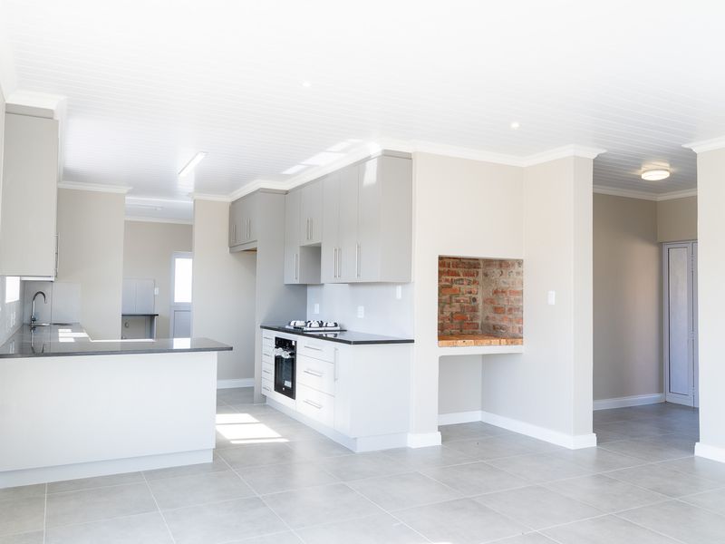 Modern open-plan kitchen featuring sleek grey cabinetry, granite countertops, integrated appliances, and a built-in indoor braai, finished with neutral tiling throughout.