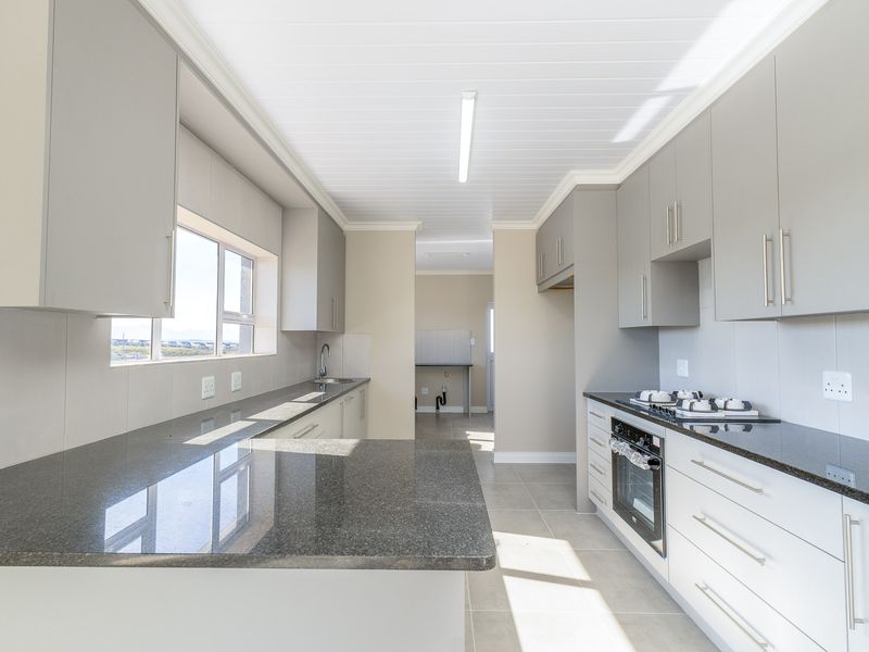 Modern kitchen featuring sleek grey cabinetry, granite countertops, built-in oven and hob, and tiled flooring in a clean, well-lit space.