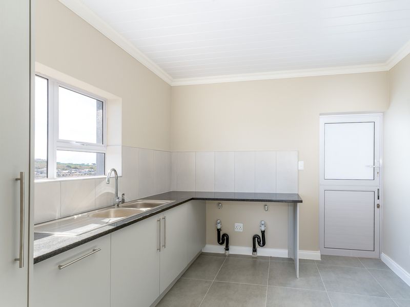 A clean and modern laundry room featuring built-in cabinetry, a stone countertop with a stainless steel sink, and direct access to the exterior.