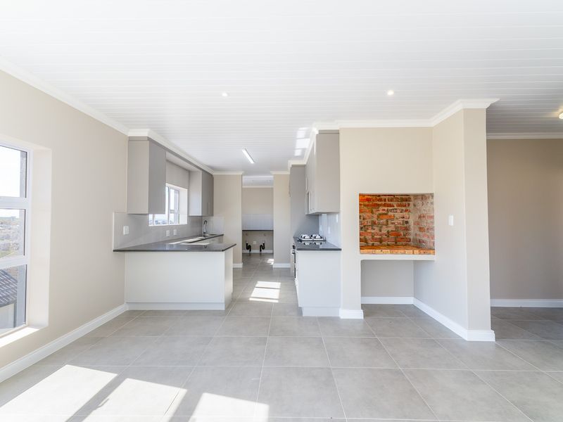 Modern open-plan kitchen featuring sleek cabinetry, stone countertops, built-in stove, and a unique exposed brick indoor braai area with neutral tiled flooring.