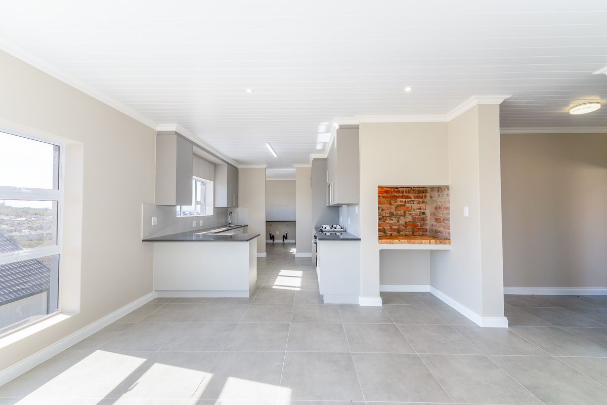 Modern open-plan kitchen featuring sleek cabinetry, stone countertops, built-in stove, and a unique exposed brick indoor braai area with neutral tiled flooring.