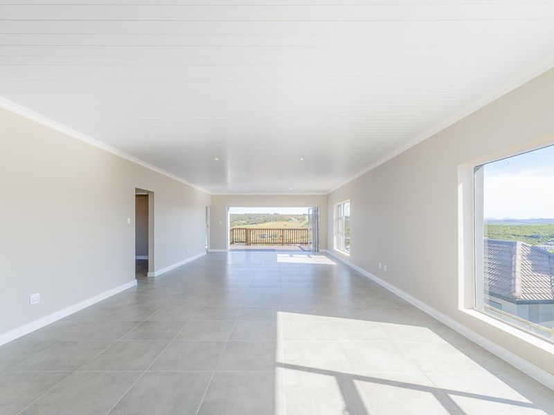 A spacious, bright, and empty living area featuring neutral tiled floors, a clean tongue and groove ceiling, and large windows with scenic views.