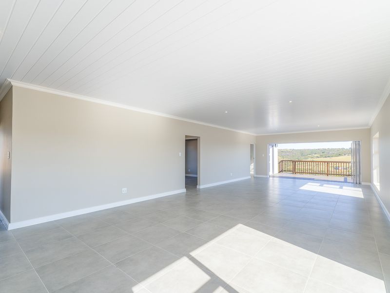 Spacious, open-plan living area featuring neutral tiled floors, a modern tongue and groove ceiling, and large bi-fold doors opening to a scenic balcony.