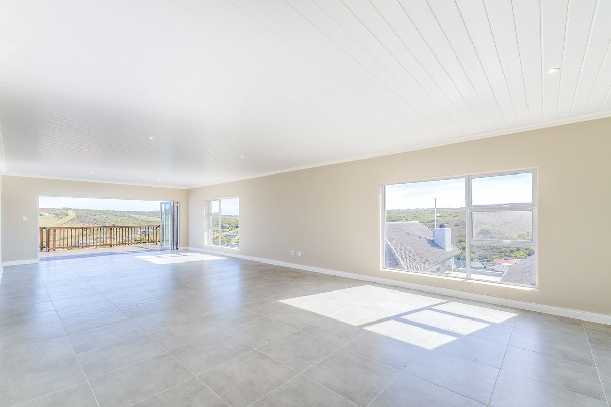 Spacious, light-filled living area featuring neutral tiled flooring, a modern tongue and groove ceiling, and large windows offering expansive views and balcony access.