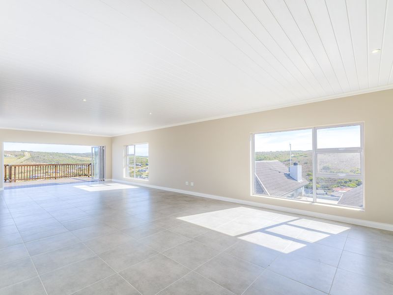 Spacious, light-filled living area featuring neutral tiled flooring, a modern tongue and groove ceiling, and large windows offering expansive views and balcony access.