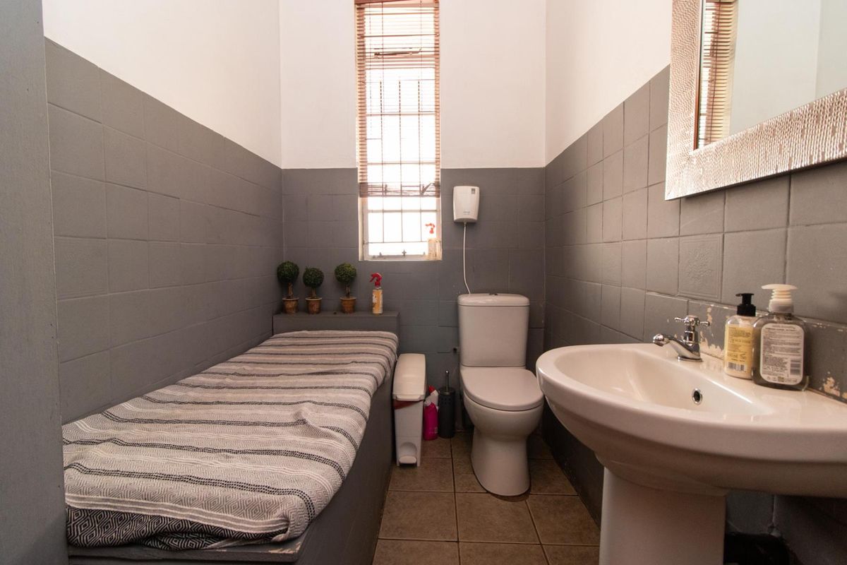 A functional bathroom featuring a pedestal washbasin, toilet, and tiled wall finishes with a window for natural light.