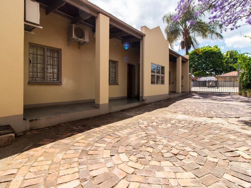 Front exterior view of the office property featuring a covered patio, brick paved driveway, and secure perimeter fencing.