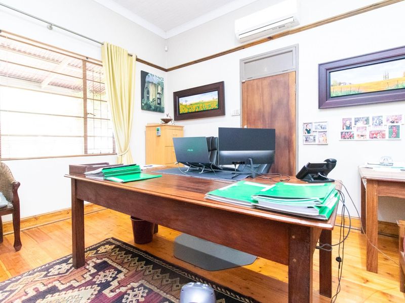 A functional office space featuring polished timber flooring, an integrated air conditioning unit, and natural light through a window with security bars.