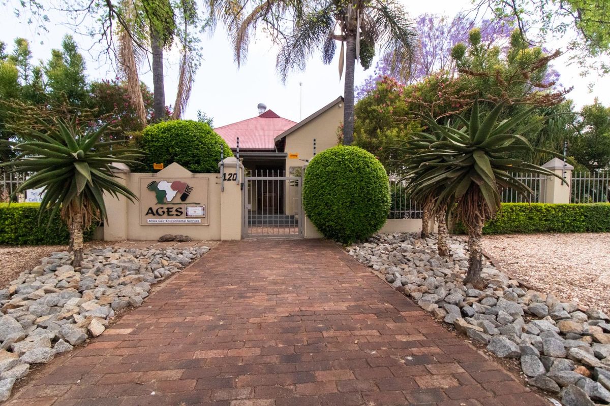 Front entrance view of the office property featuring a brick paved walkway, secure metal gate, perimeter wall with electric fencing, and established garden.