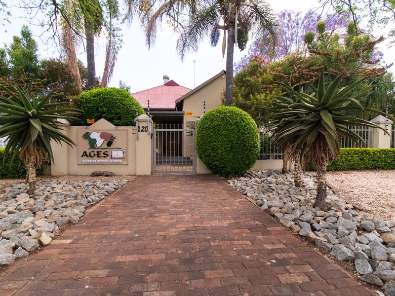 Front entrance view of the office property featuring a brick paved walkway, secure metal gate, perimeter wall with electric fencing, and established garden.