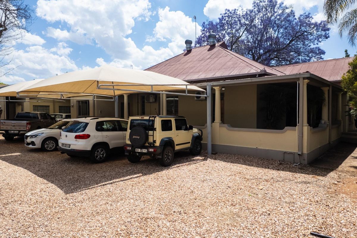 Exterior view of an office building featuring a gravel parking area with a shade sail carport and a covered veranda entrance.