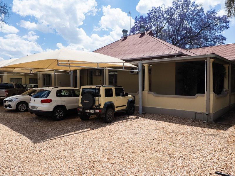 Exterior view of an office building featuring a gravel parking area with a shade sail carport and a covered veranda entrance.