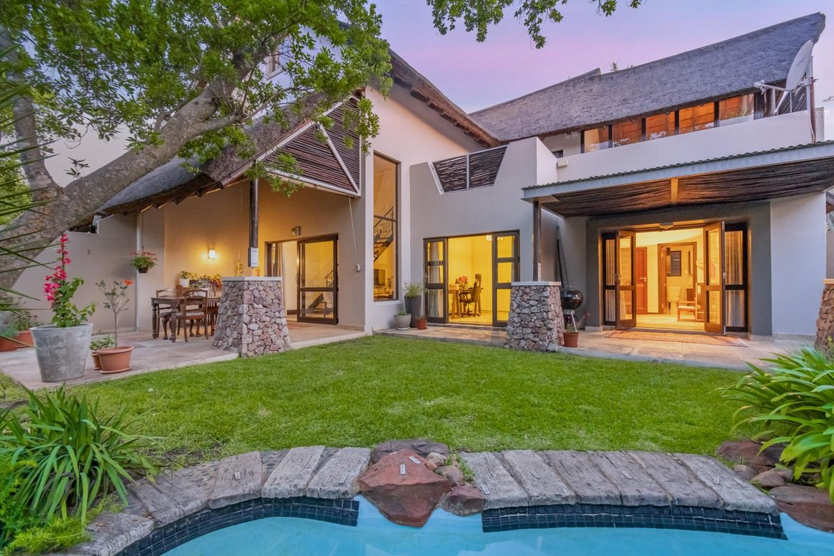 Rear view of a townhouse featuring a thatched roof, covered patio areas, and a swimming pool set within a landscaped garden.