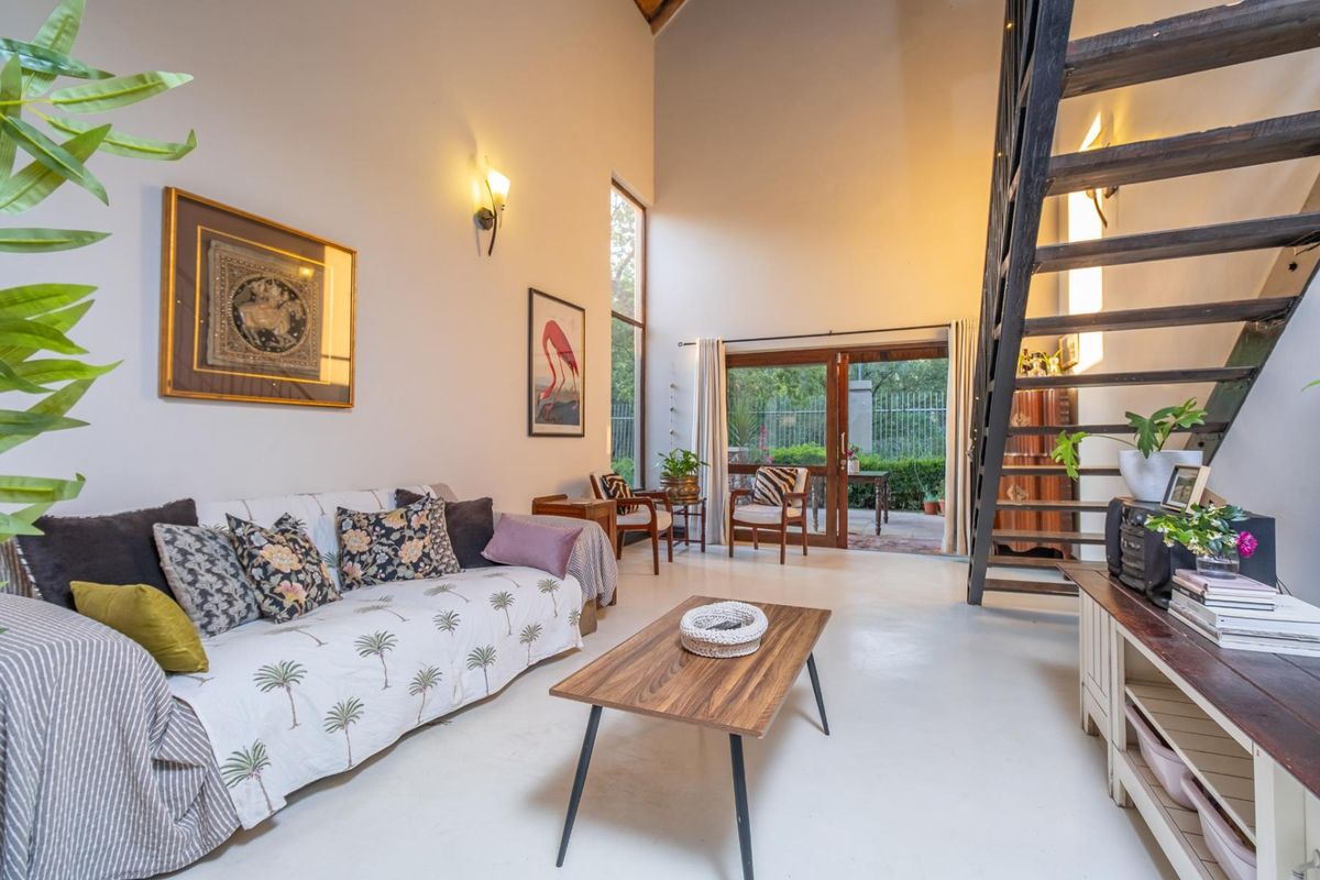 Spacious double-volume living room featuring an exposed timber staircase, tiled flooring, and large sliding glass doors providing access to the patio.