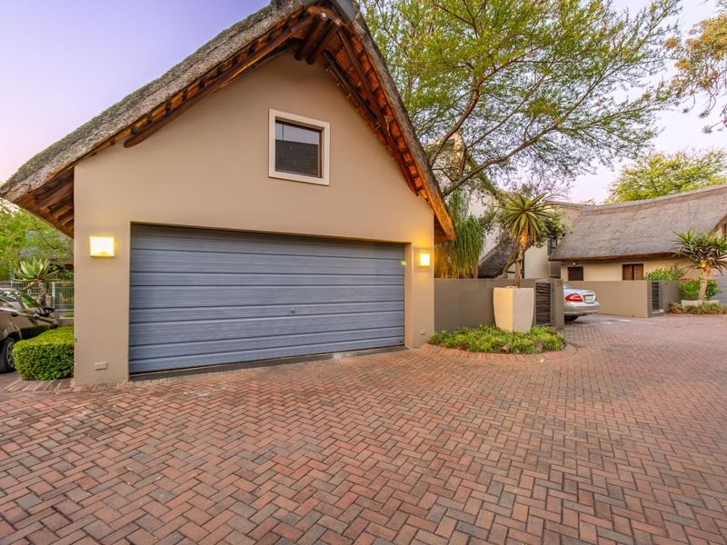 A well-maintained townhouse garage featuring a traditional thatched roof and a paved driveway entrance.