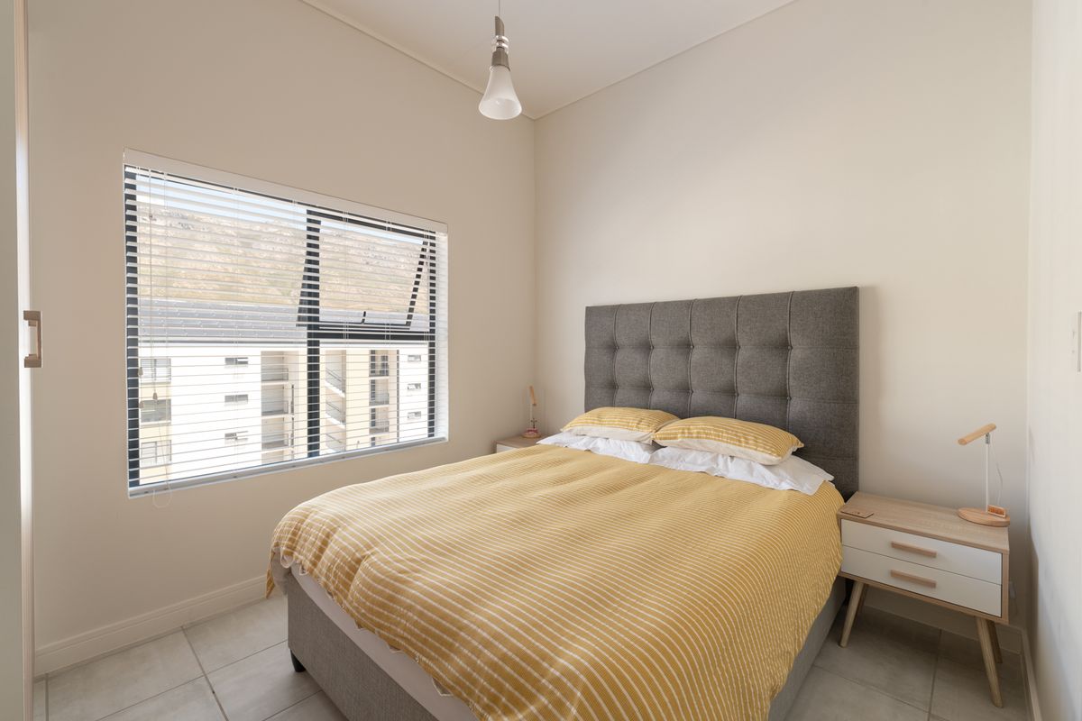 A well-maintained bedroom featuring neutral walls, tiled flooring, and a large window with venetian blinds, providing ample natural light.