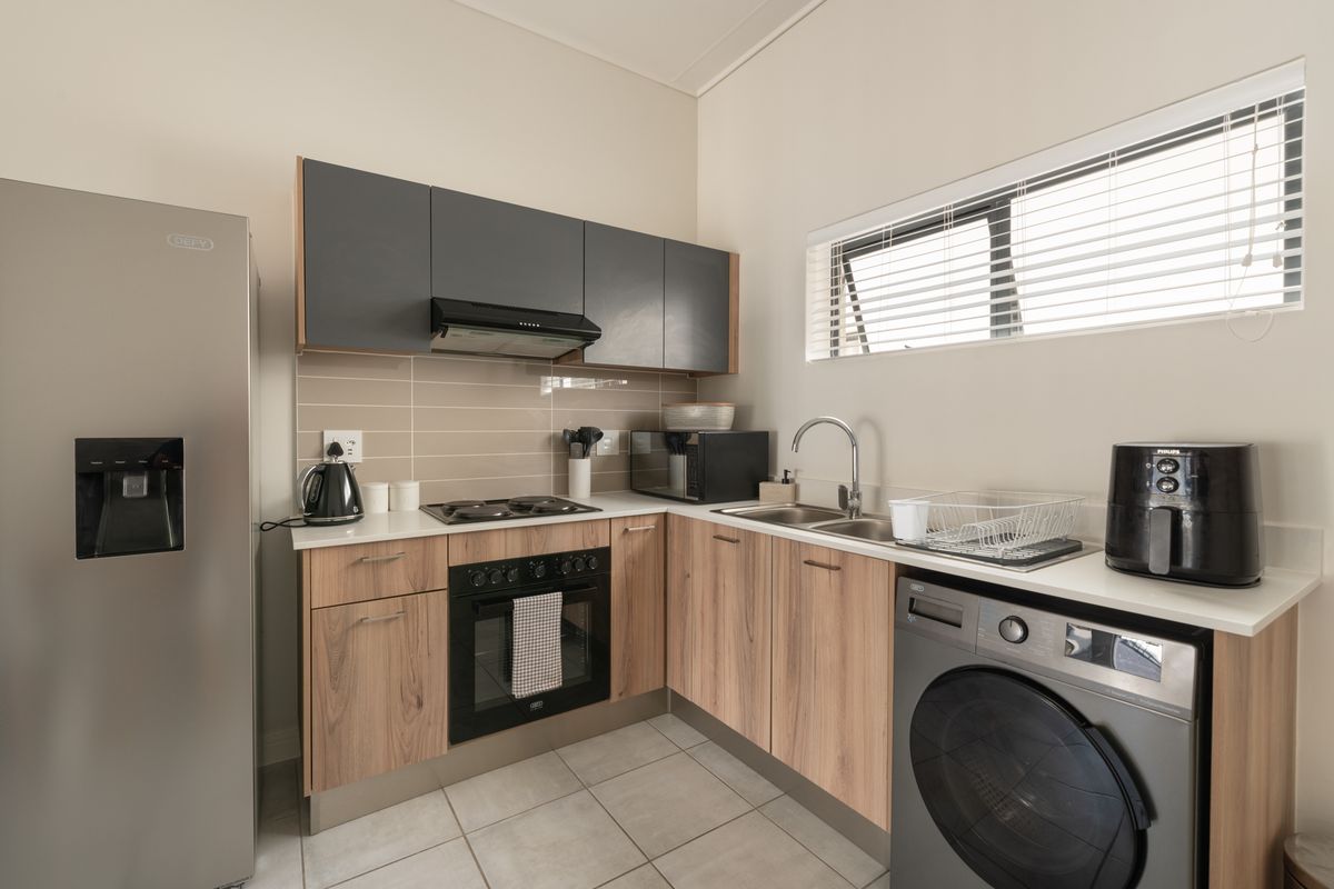 A modern, well-maintained kitchen featuring wood-finish lower cabinetry, dark grey upper cabinets, integrated appliances, and a tiled backsplash with a functional layout.