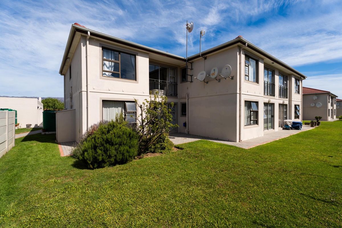 Rear view of a multi-story apartment complex featuring paved patio areas, landscaped lawns, and exterior building finishes.