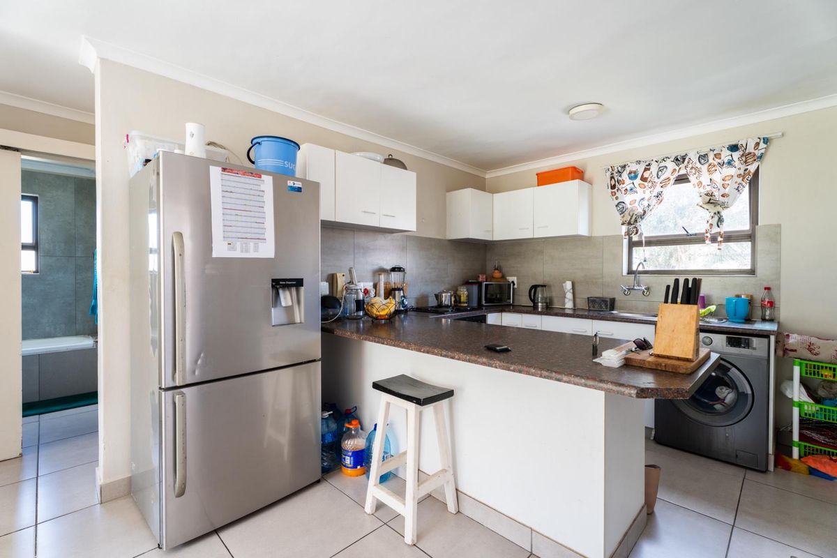 A functional kitchen featuring white cabinetry, laminate countertops, tiled backsplash, and integrated laundry plumbing, with a view into the adjacent bathroom.