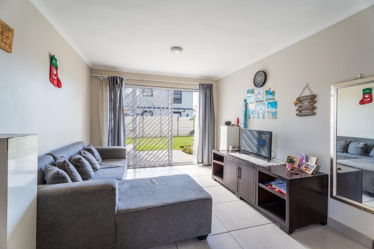 A bright living room featuring tiled flooring and a sliding glass door that provides direct access to the outdoor patio and garden area.