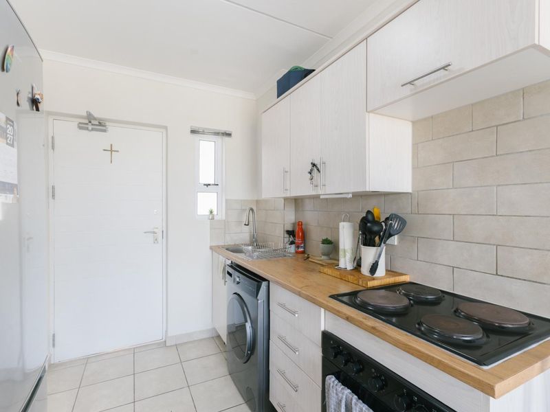 Compact kitchen featuring white cabinetry, wooden countertops, subway tile backsplash, and integrated electric hob and oven.