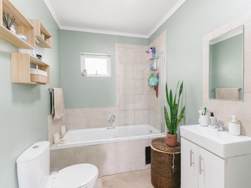 A well-maintained bathroom featuring a built-in bathtub with a glass screen, a vanity unit with a basin, and a wall-mounted mirror.