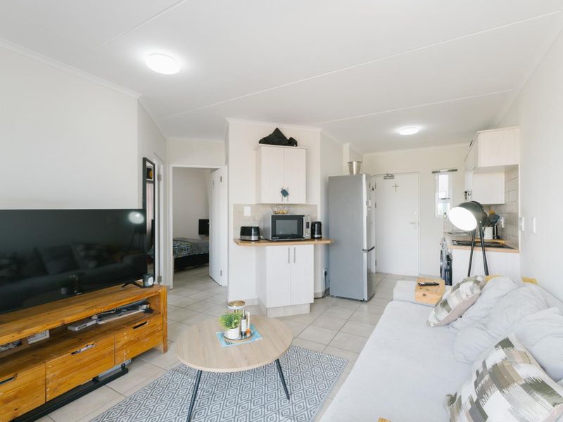 An open-plan living and kitchen area featuring tiled flooring, neutral cabinetry, and a functional layout connecting to the bedroom.