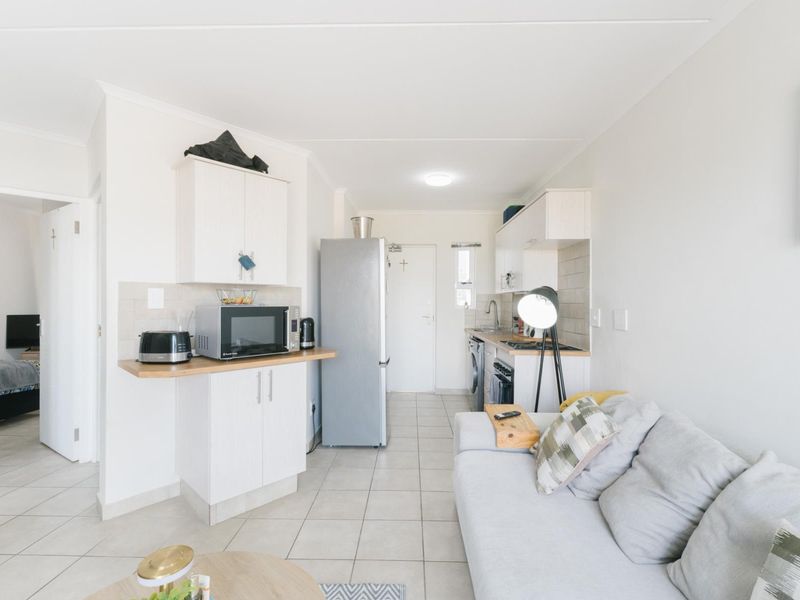 An open-plan living and kitchen area featuring tiled flooring, white cabinetry, and integrated kitchen appliances, creating a functional and compact living space.