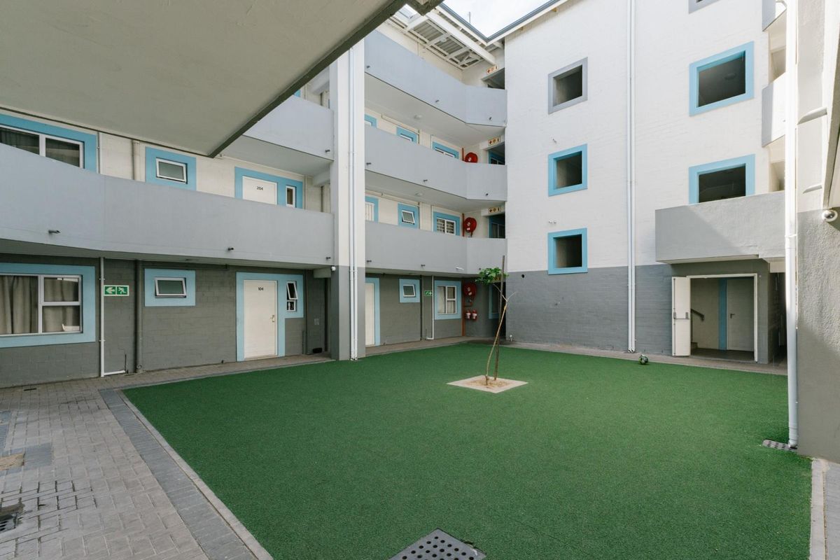 A central courtyard area within an apartment complex featuring artificial turf, paved walkways, and multi-level access balconies with fire safety equipment.