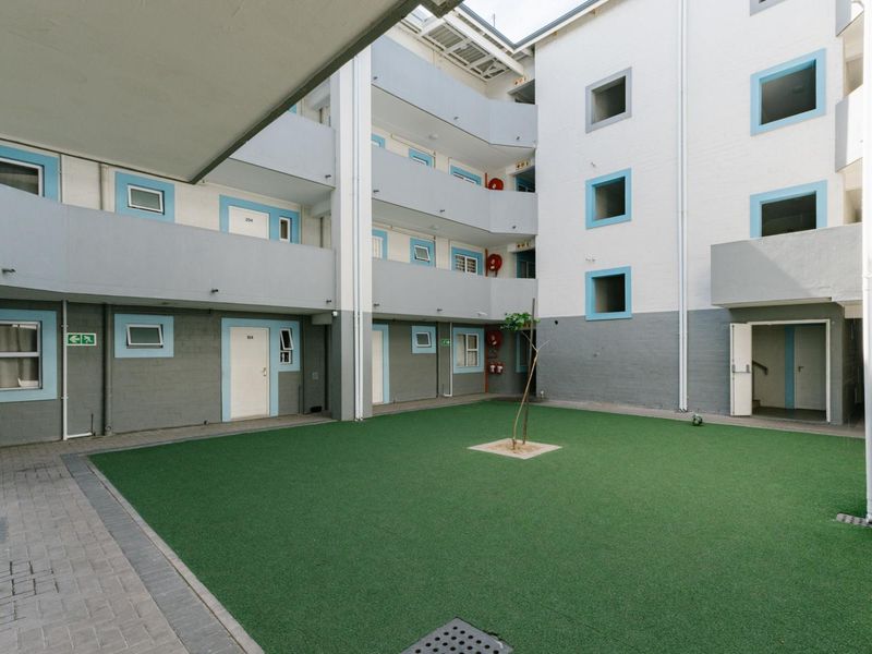 A central courtyard area within an apartment complex featuring artificial turf, paved walkways, and multi-level access balconies with fire safety equipment.