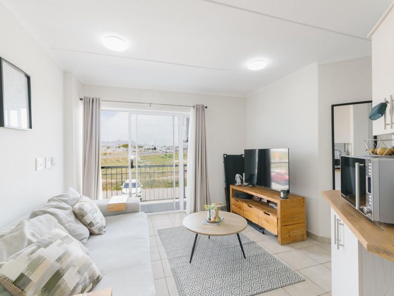 Bright open-plan living area featuring tiled floors, modern kitchen cabinetry, and a sliding glass door leading to a balcony with scenic views.