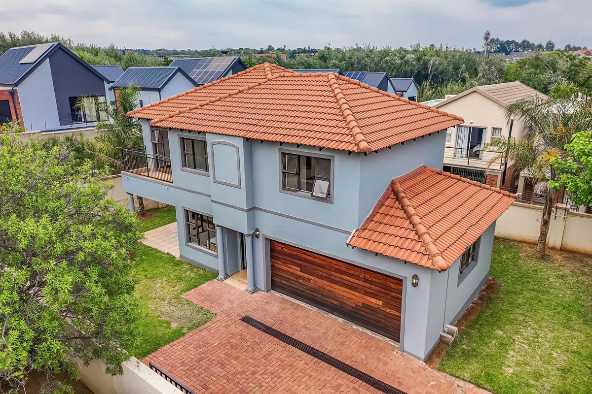 Aerial view of a two-story residential house featuring a terracotta tiled roof, a wooden double garage door, and a brick-paved driveway.
