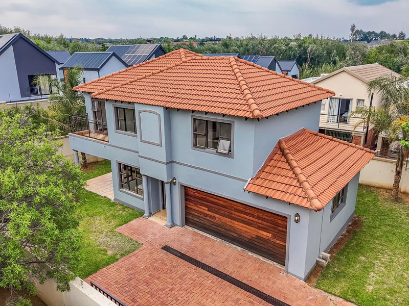 Aerial view of a two-story residential house featuring a terracotta tiled roof, a wooden double garage door, and a brick-paved driveway.
